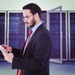Biznesmen przewijający się na swoim cyfrowym tablecie przed wieżami serwerów