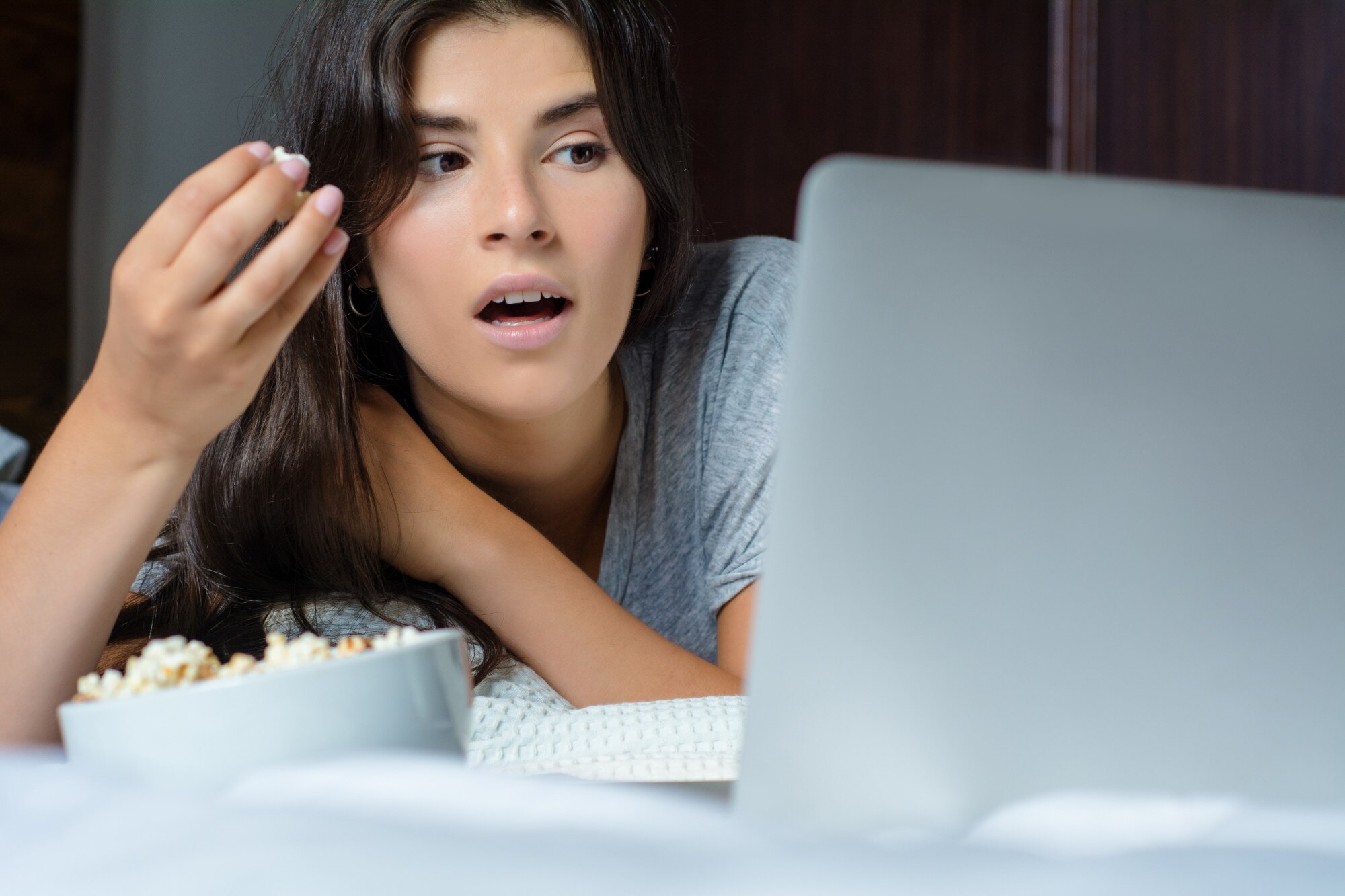Młoda kobieta używa laptop i jedzący popkorn
