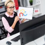 Młoda dziewczyna ze słuchawkami siedzi przy stole komputera i trzyma arkusz na schemacie.