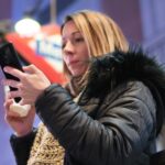 Ładna młoda kobieta z smartphone i kawowy ono uśmiecha się szczęśliwy w mieście przy nocą.